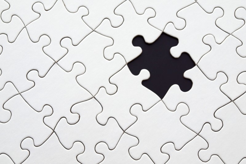 A white jigsaw with a black gap where a piece is missing 